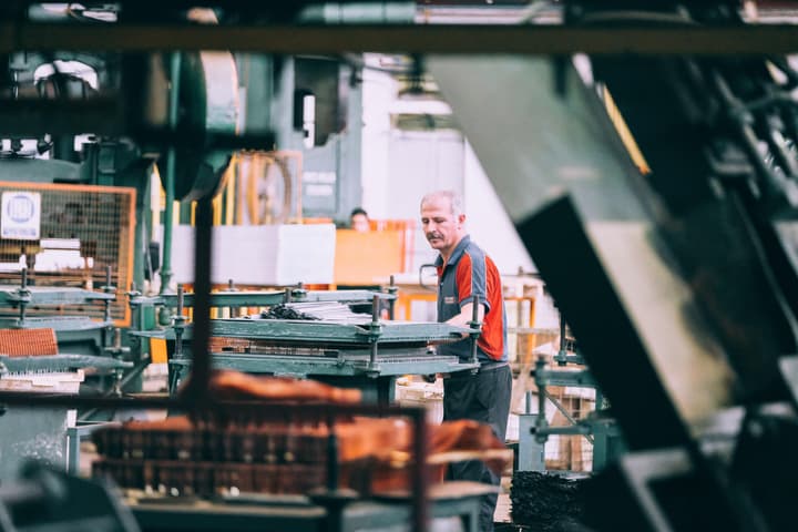 White older man with greying hair examines product in a manufacturing facility. Image by Sam Moghadam Khamseh via Unsplash.
