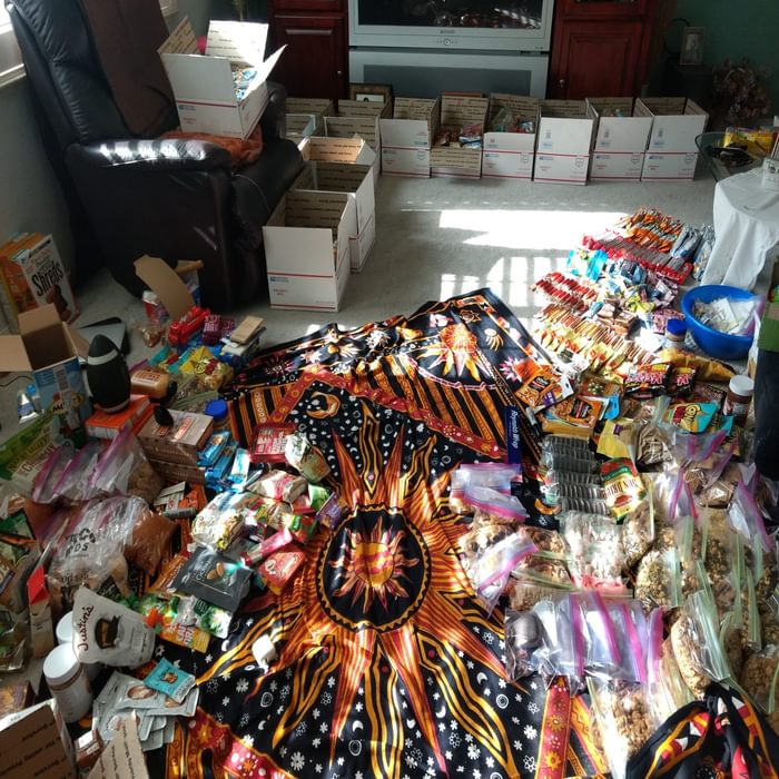 Resupply boxes: Food representing roughly 60 days of hunger prevention spreads across the living room floor before being carefully packaged in resupply boxes.