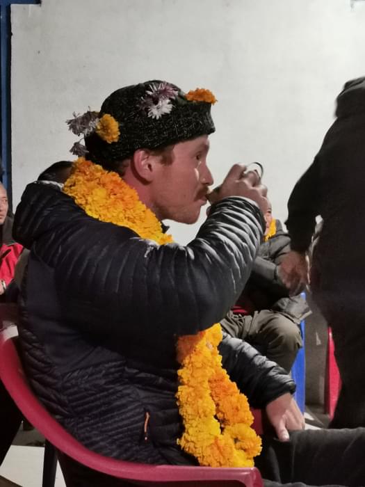 A member of our group sits like a king; covered in marigold garlands and drinking rice wine