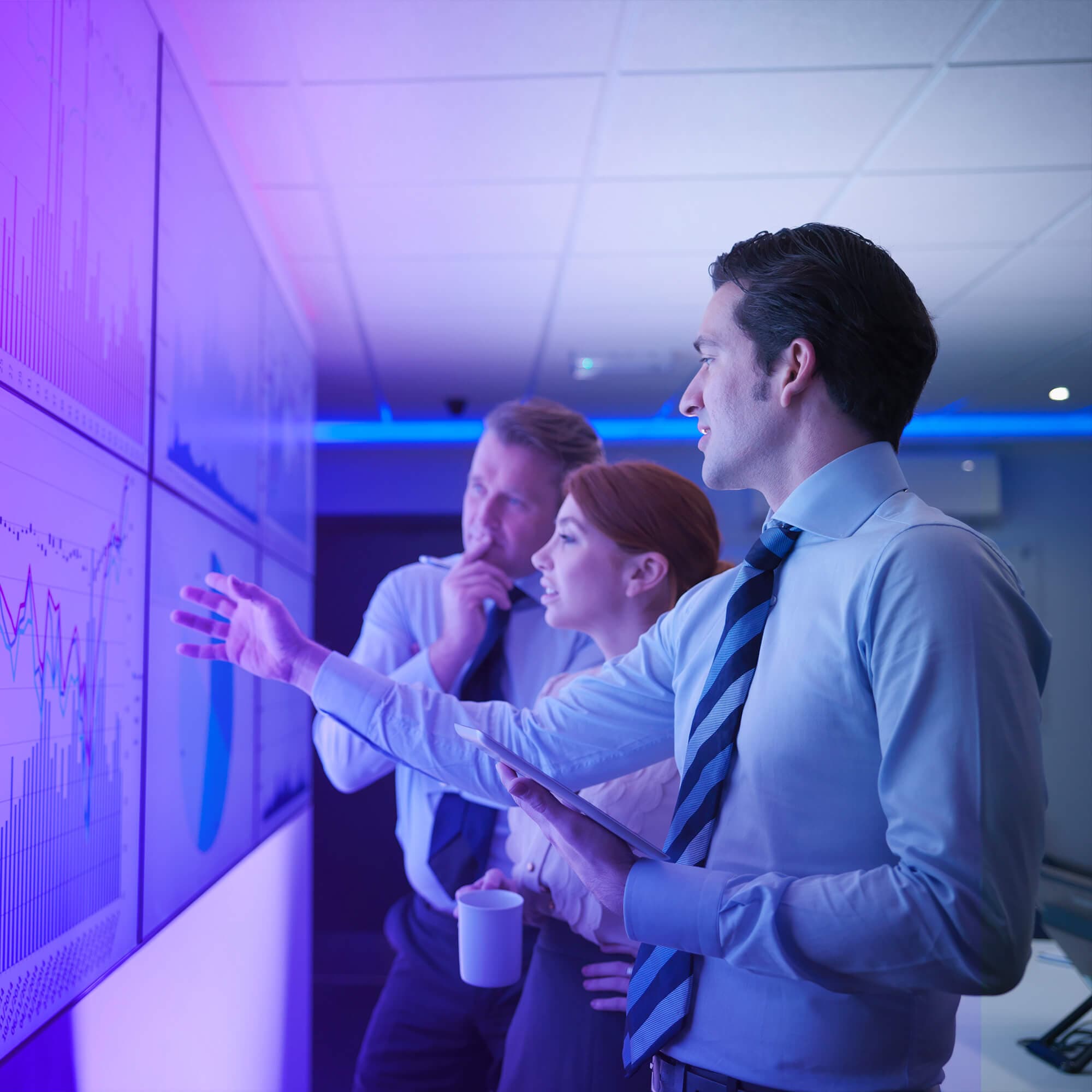 Woman and two men viewing data on a wall of screens