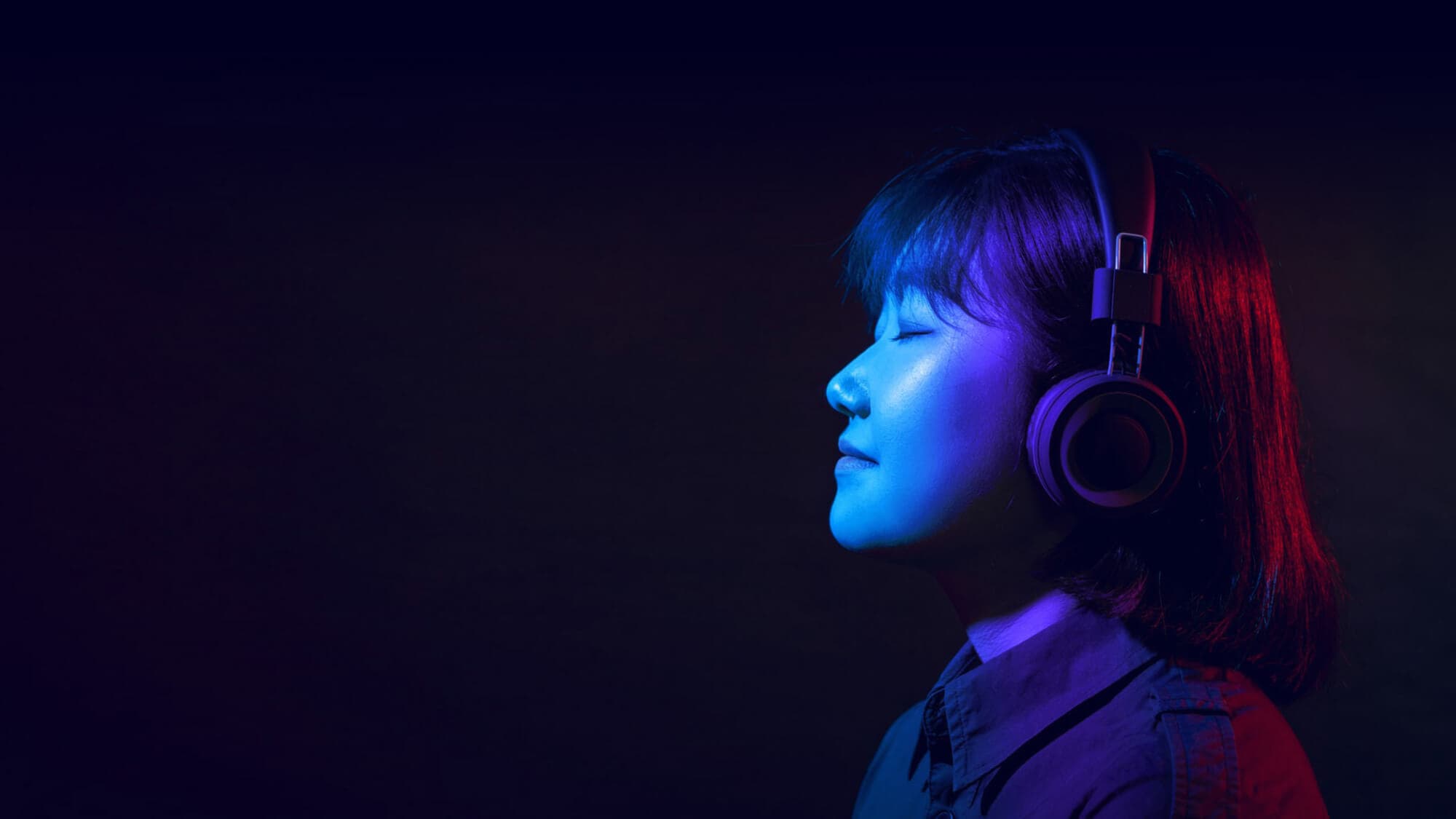 A woman wearing headphones in front of a dark background.