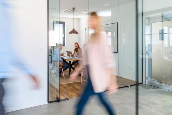 woman walking past an meeting room where people are gathered