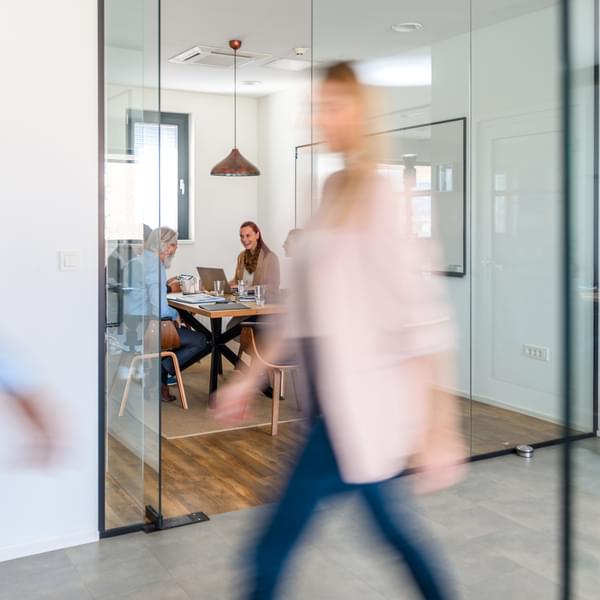 woman walking past an meeting room where people are gathered