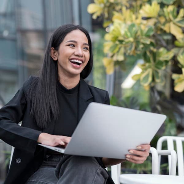 woman sitting on a park bench and smiling while holding a laptop