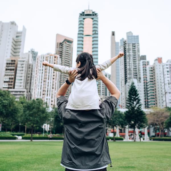Rear view of young Asian father carrying happy little daughter on shoulders in urban park