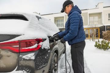 Beautiful view of a man connecting a charging cable to an electric car charging station on a frosty winter day