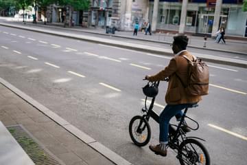 A behind view of a young businessman casually riding his electric bicycle to work through the city.