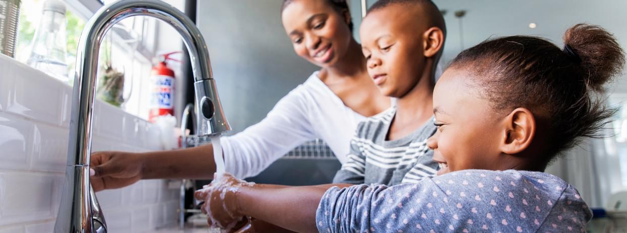Mother opening the tap for her kids to wash their hands in the kitchen.
