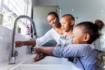 Mother opening the tap for her kids to wash their hands in the kitchen.