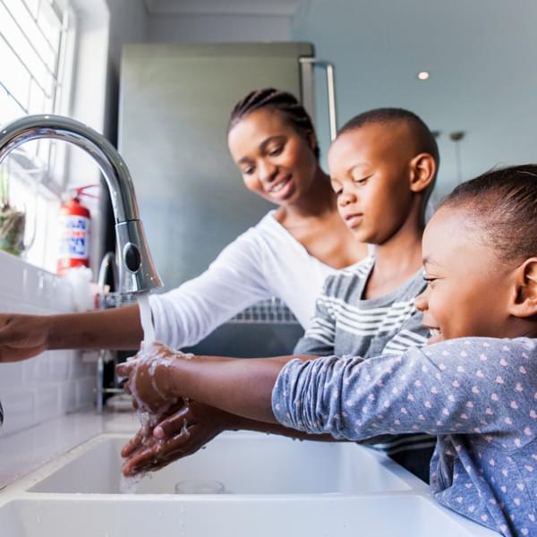 Mother opening the tap for her kids to wash their hands in the kitchen.