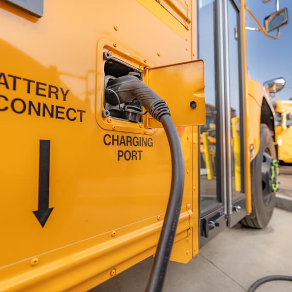 Yellow electric school bus plugged in at a charging station.