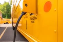 Yellow electric school bus plugged in at a charging station.