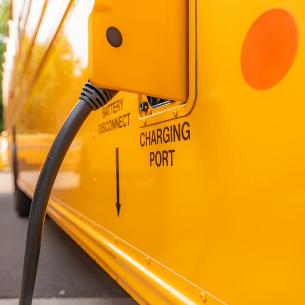 Yellow electric school bus plugged in at a charging station.