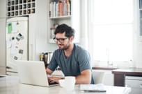 Shot of a young man using a laptop while having breakfast in the kitchen at home