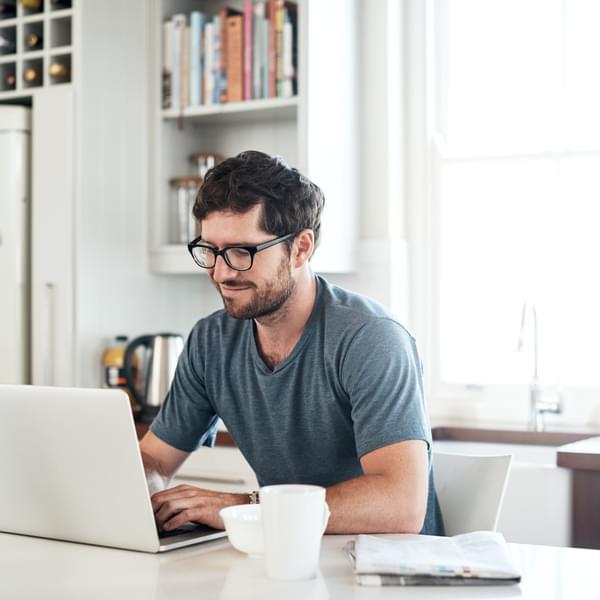 Shot of a young man using a laptop while having breakfast in the kitchen at home