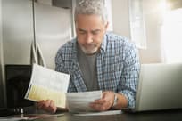 Hispanic man paying bills on laptop in kitchen