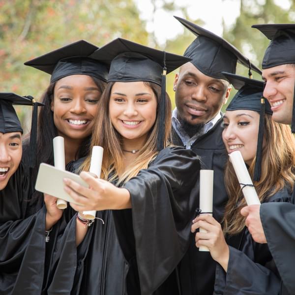 Multi-ethnic group of college student friends take selfie photos with cell phone after graduation ceremony.