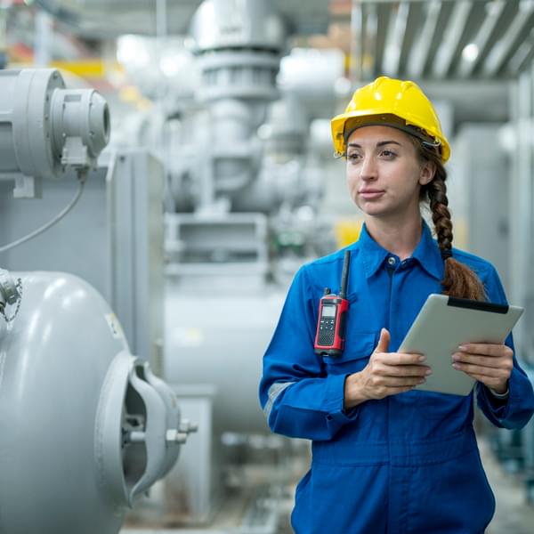 Female stationary engineer working at industrial mechanical room, examining the operation of the ventilation system in the factory.