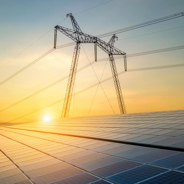 High voltage pylons with electric power lines transferring electricity from solar photovoltaic cells at sunrise.