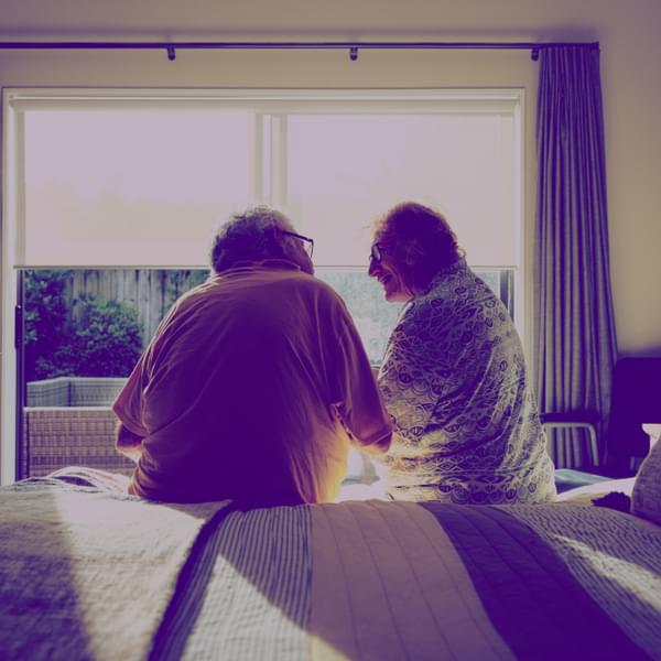 Back shot of senior couple sitting on edge of bed, in front of window