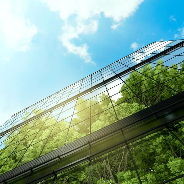 Image of business building with reflection of green trees and blue sky.