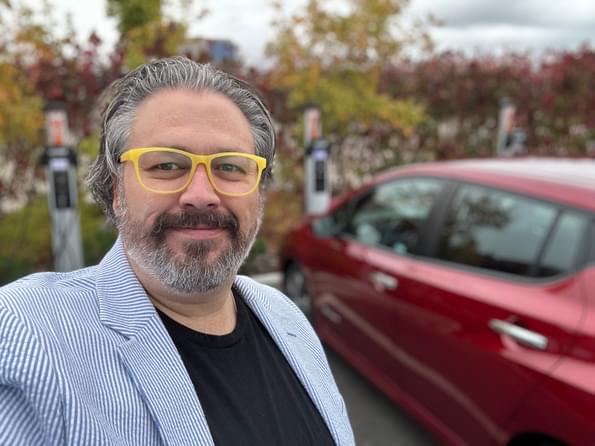 Resource Innovations employee posing in front of his electric car (EV)