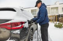 Beautiful view of a man connecting a charging cable to an electric car charging station on a frosty winter day