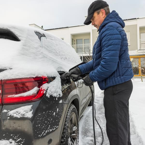 Beautiful view of a man connecting a charging cable to an electric car charging station on a frosty winter day