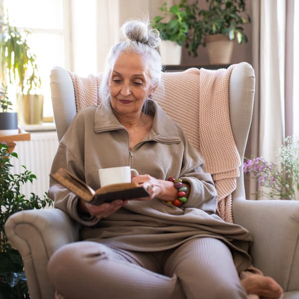 Relaxed senior woman sitting in armchair and reading book indoors at home.