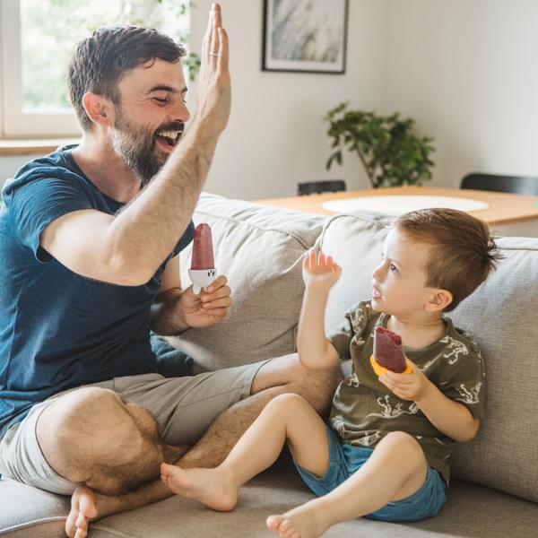 Father sitting on sofa with his young son eating popsicles. They are happy and excited about being together.