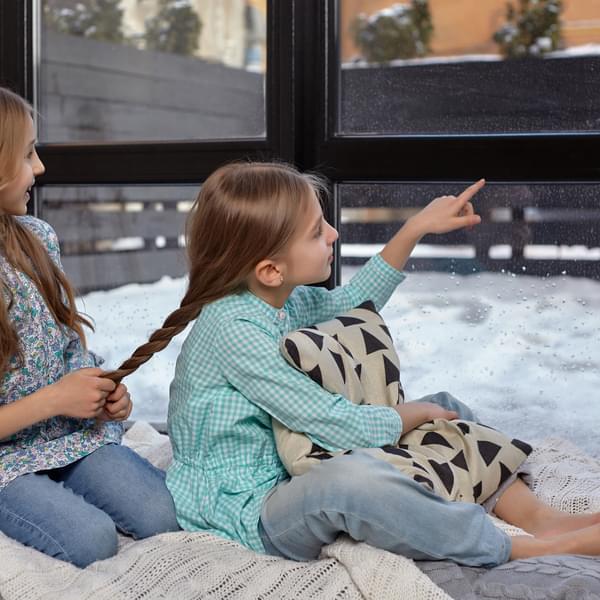 Two little sisters sitting on windowsill, looking at the window while braiding hair