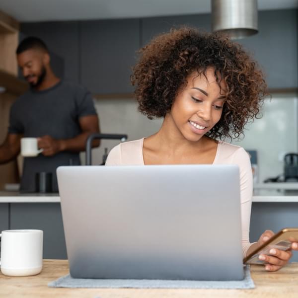 African American woman at home working online on a laptop and her cell phone