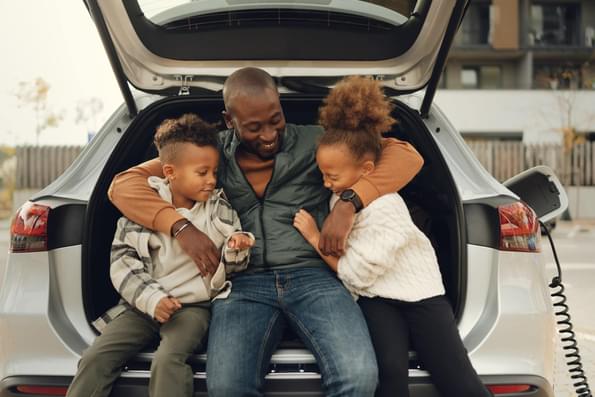 Happy family sitting on the bumper of their electric vehicle