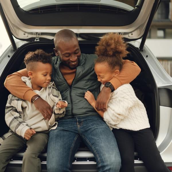 Happy family sitting on the bumper of their electric vehicle