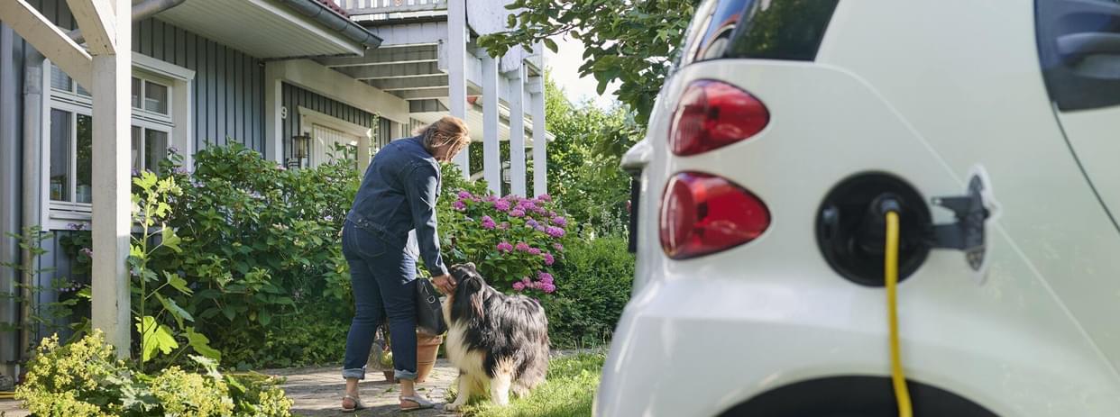 Woman walking to entrance of her house while her electric car is charging