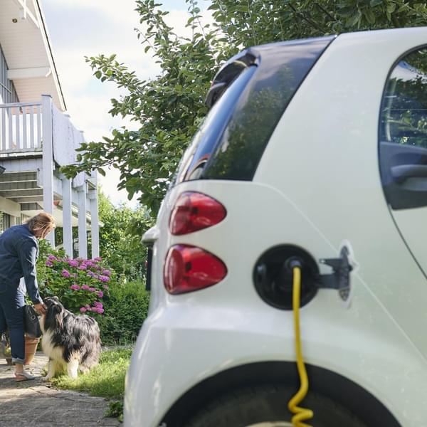 Woman walking to entrance of her house while her electric car is charging