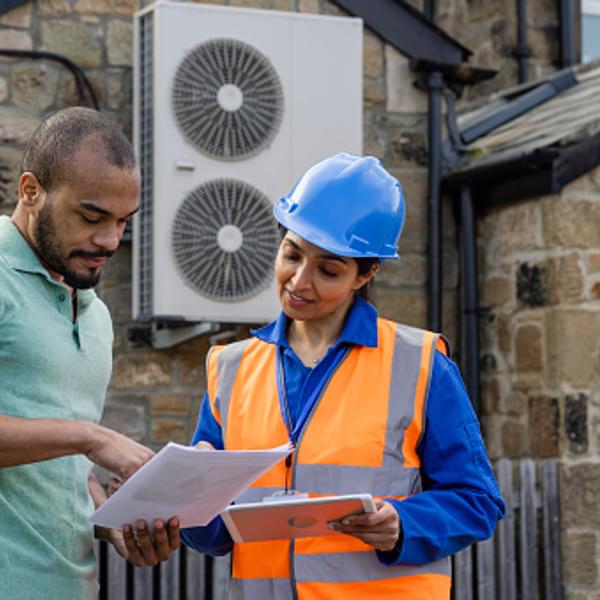 Engineer in hardhat and bright orange vest standing outside reviewing documents with a customer