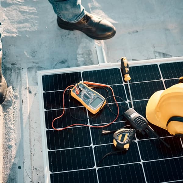 Engineer standing next to solar panels with a yellow hard had and equipment on the ground