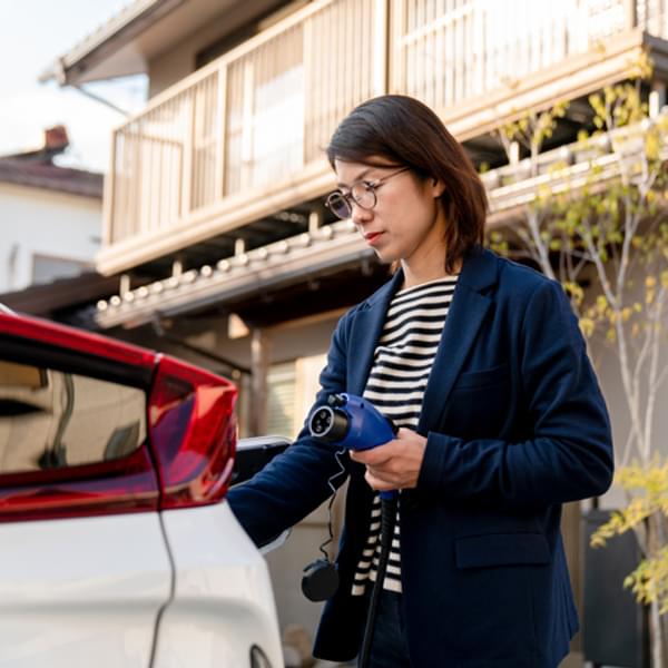 Asian woman charging her electric vehicle at home.