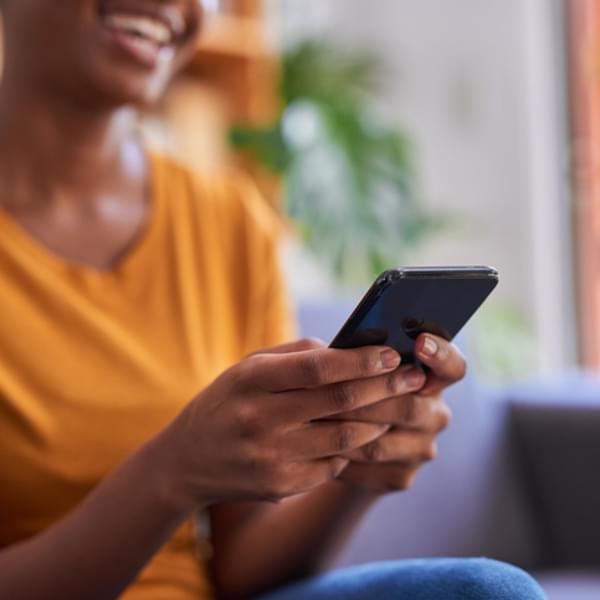 A close up cropped shot of a mobile phone being held by a young woman at home.