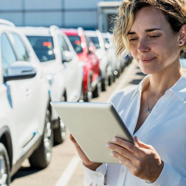 Portrait of woman taking inventory on digital tablet in parking lot with cars.