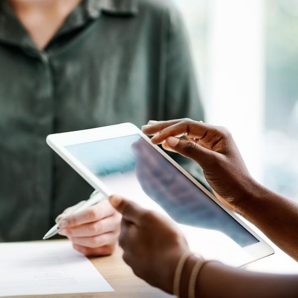 Two businesswomen sitting at desk in office using digital tablet.