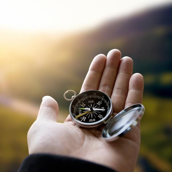 Traveler explorer man holding compass in a hand in mountains at sunrise, point of view