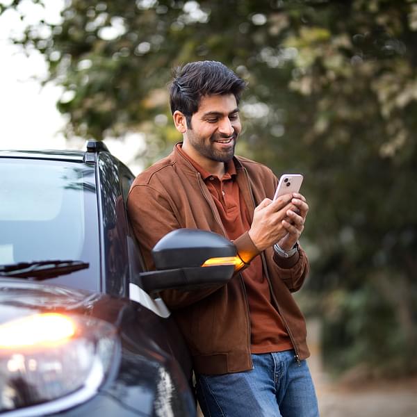 Smiling young man using mobile phone leaning on his electric car.