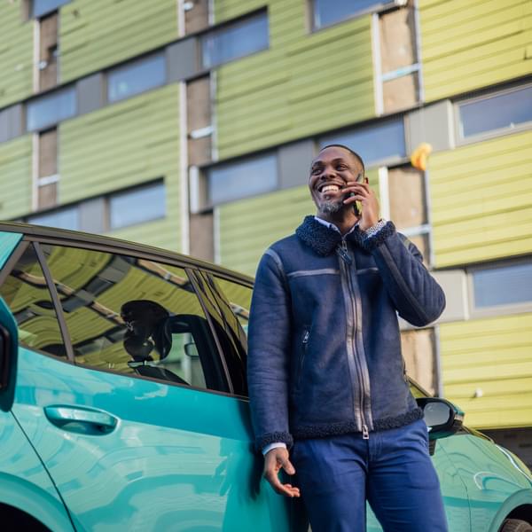 Businessman taking a phone call on his smartphone while his electric car is on charge at a public charging point.