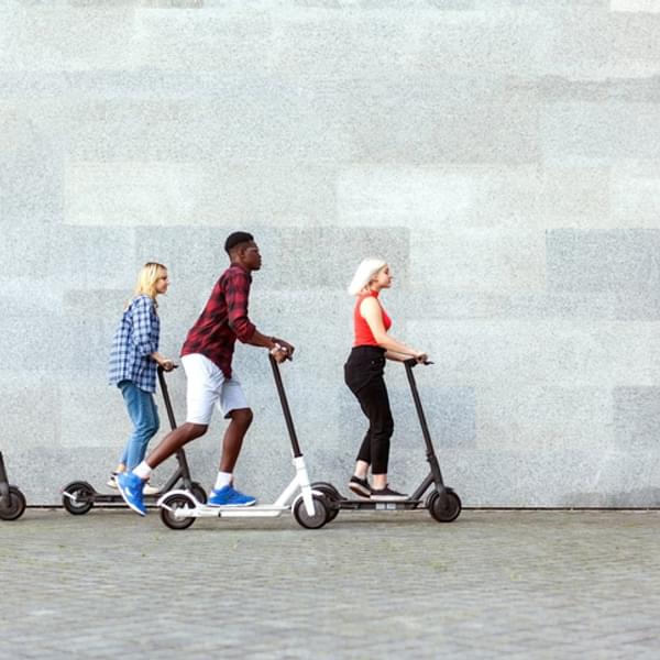 Friends rides electric scooters against the background of a wall, young people use eco transport in the city