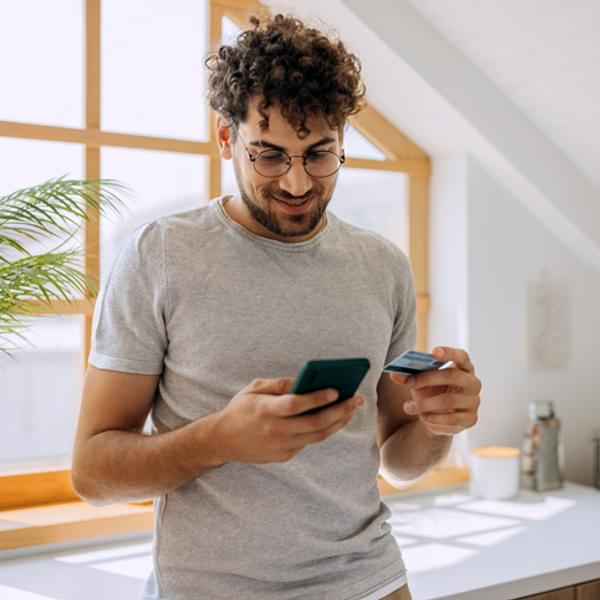 Young casually clothed man online shopping from her domestic kitchen, he is using smart phone
