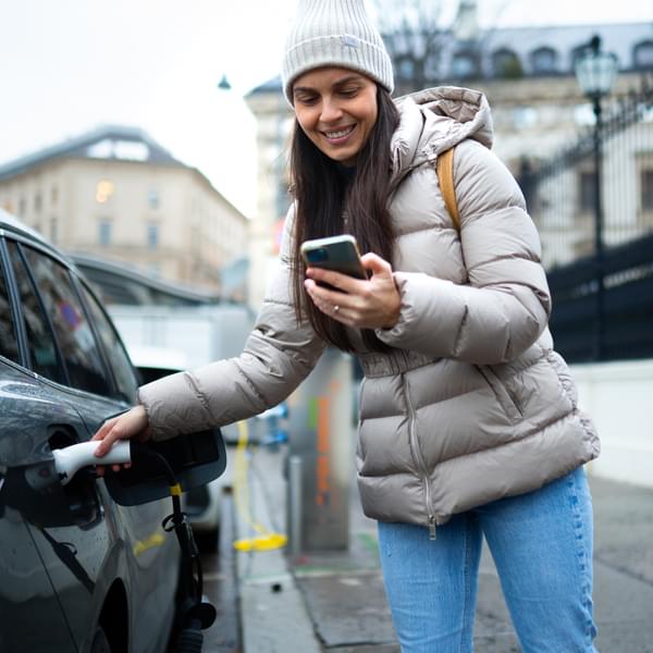 Woman in a winter jacket using her mobile phone while waiting for her electric car to charge.