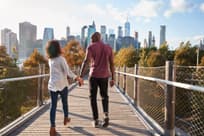 Couple walking on bridge with New York City skyline ahead.