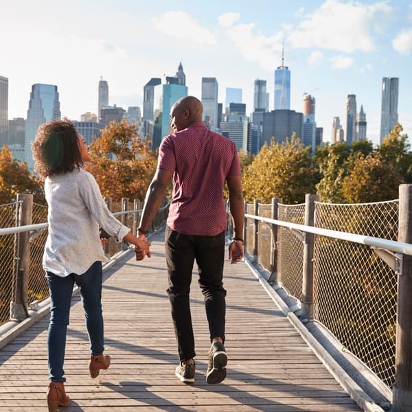 Couple walking on bridge with New York City skyline ahead.